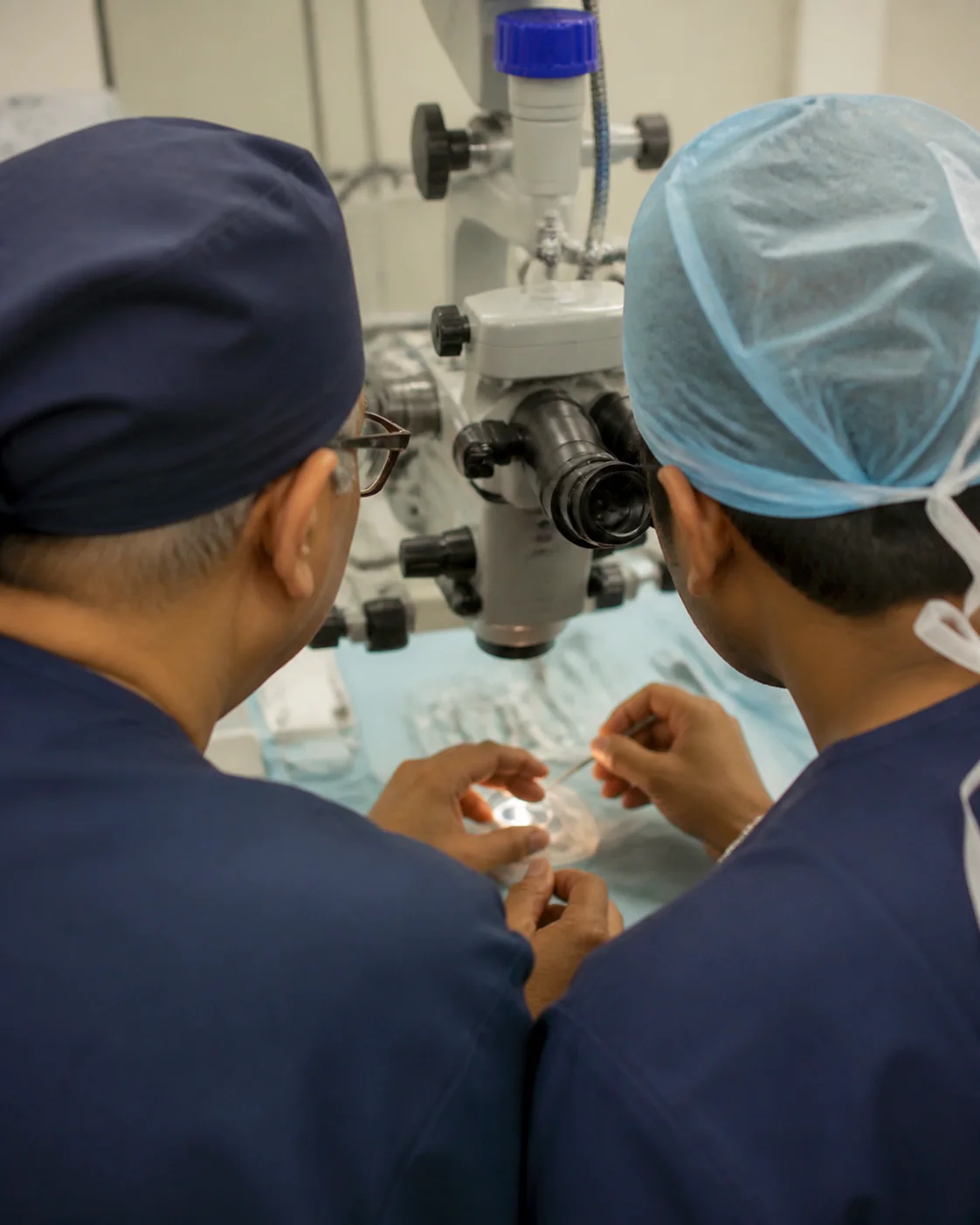 A surgeon seen from behind while teaching at a microscope, without showing a likeness.